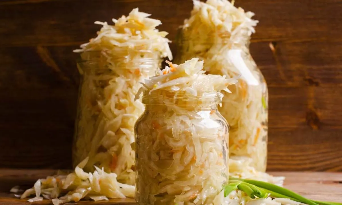 Three glass jars overflowing with fermented sauerkraut on a rustic dark wood surface, with green onions beside them