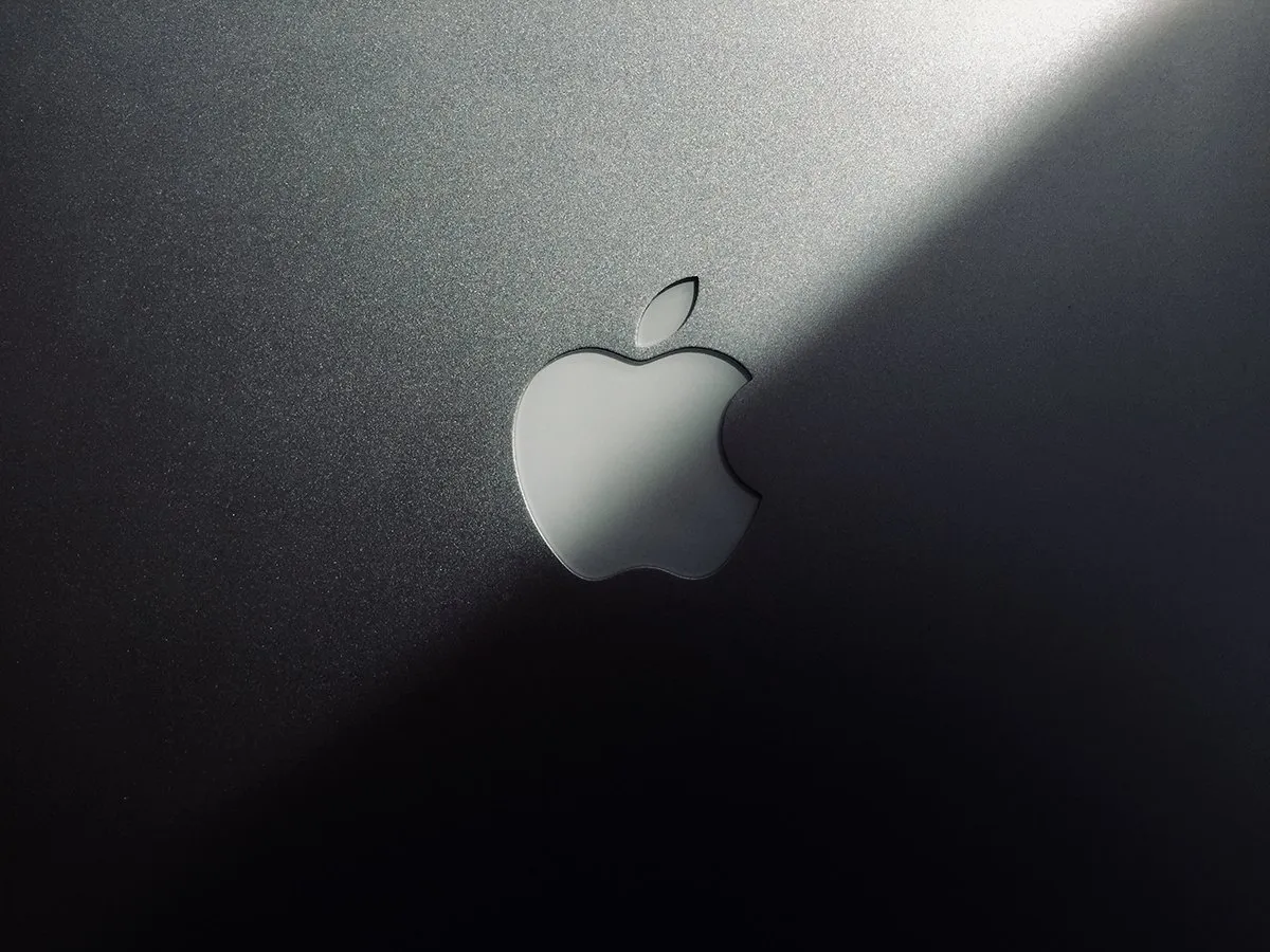 Close-up of the silver Apple logo on a brushed-metal laptop lid catching a diagonal beam of light