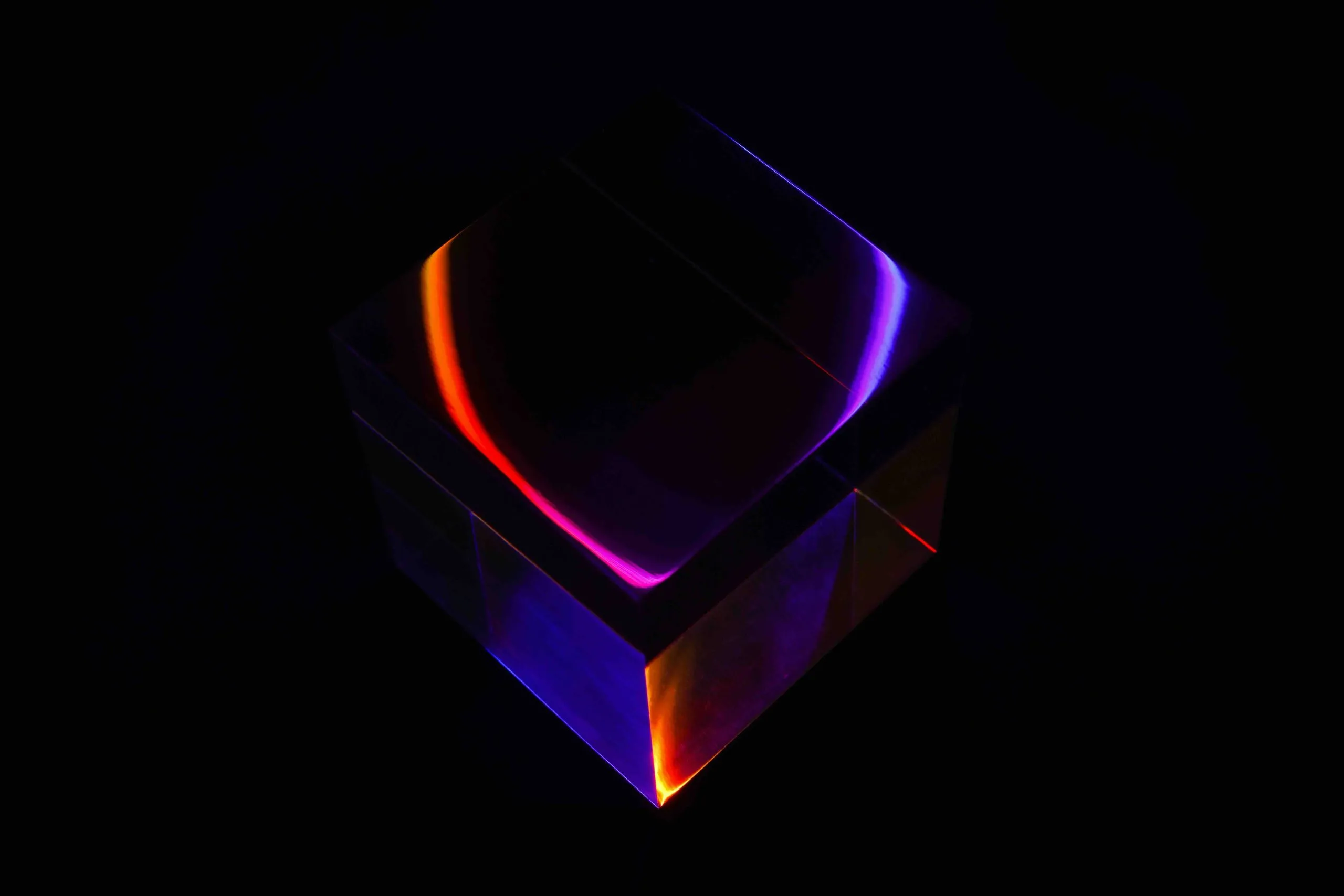 Glass cube refracting orange and purple light against a pure black background