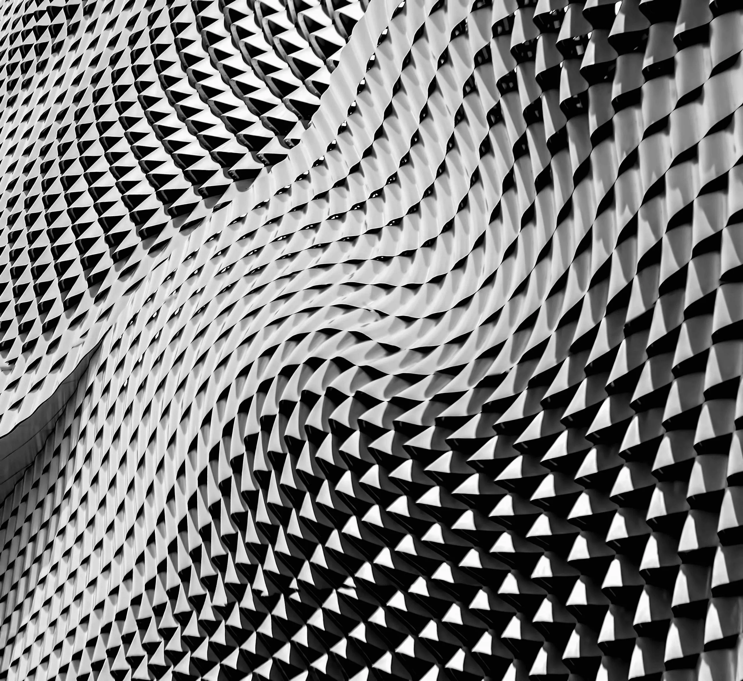 Black-and-white abstract architectural facade of tightly packed triangular fins swirling in a vortex pattern