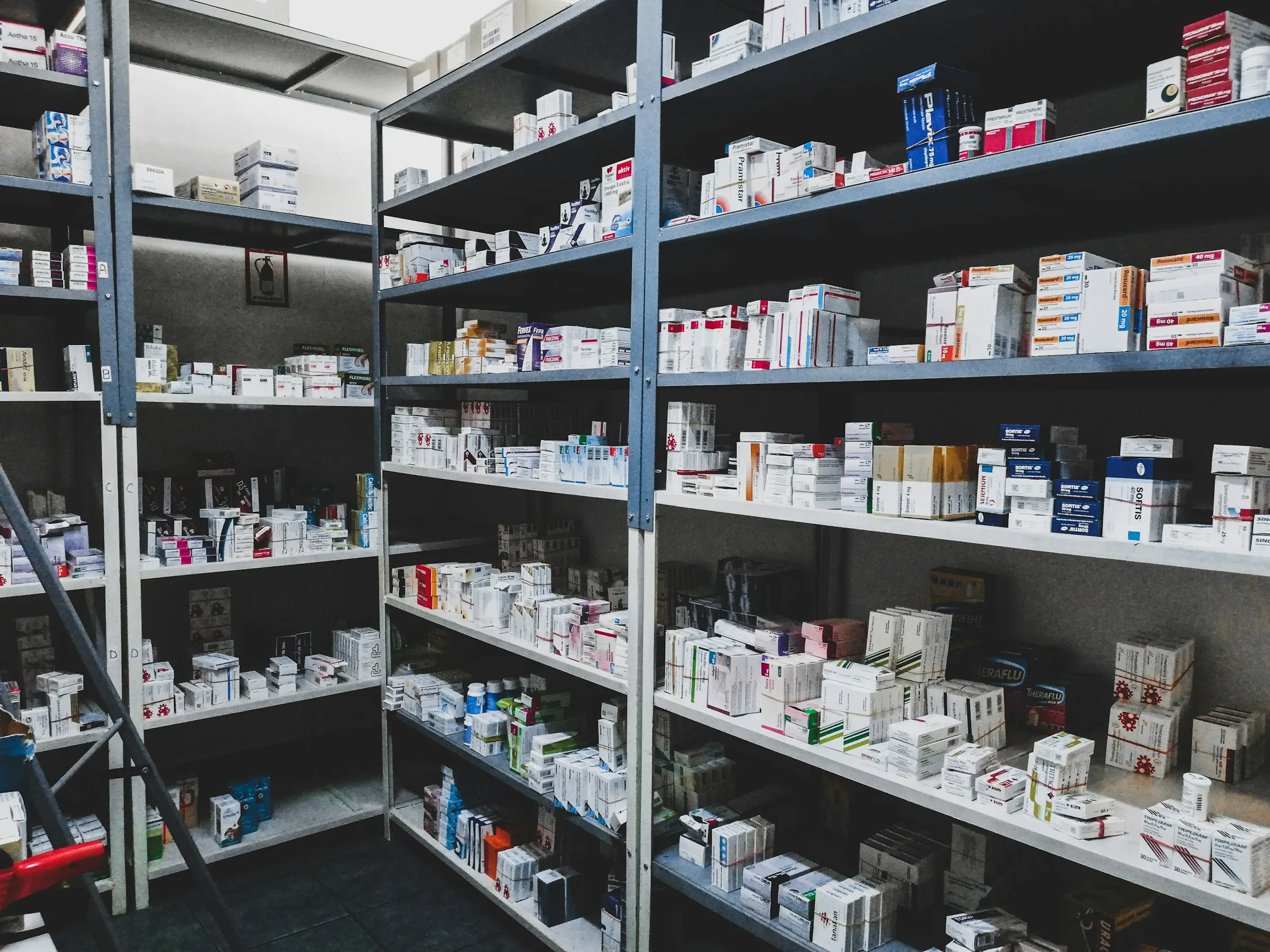 Pharmacy stockroom with metal shelving packed full of boxed medications and product cartons
