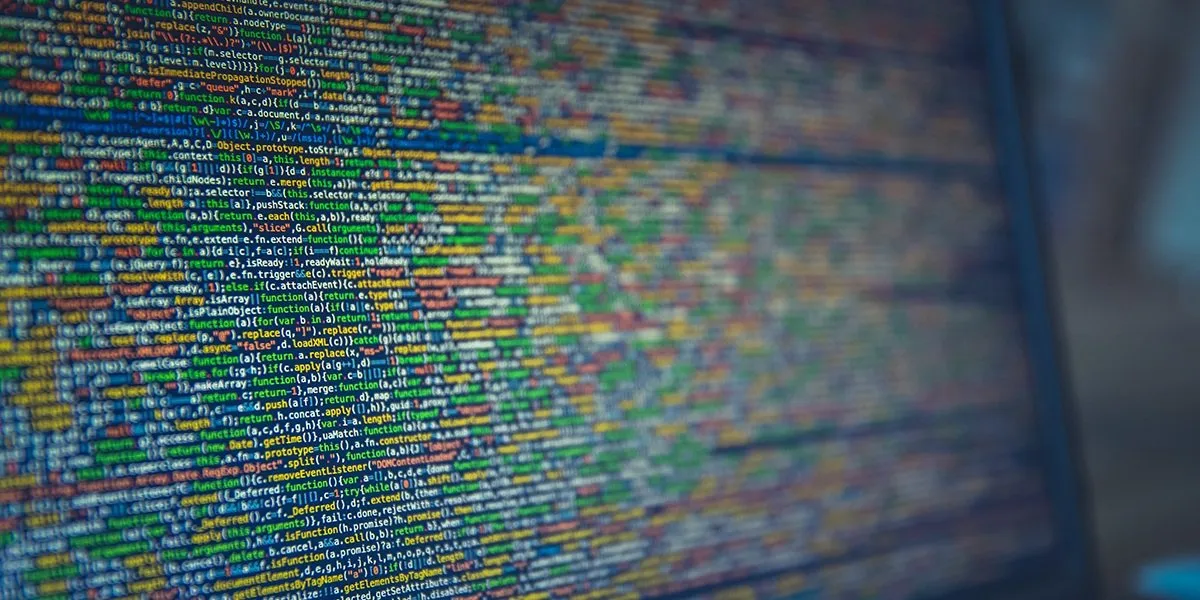 A computer screen filled with dense, colorful minified JavaScript source code viewed at an angle