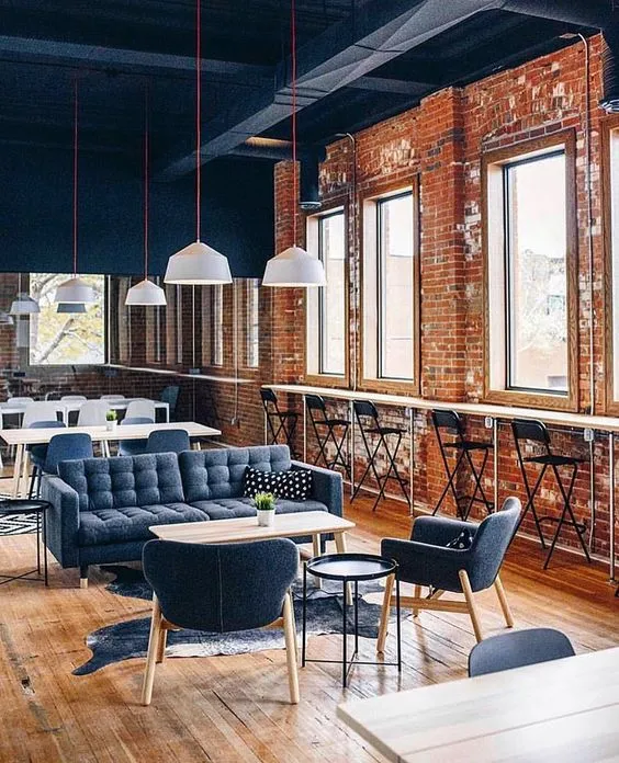 Coworking interior inspiration — exposed-brick loft lounge with navy sofa, pendant lights and high stools