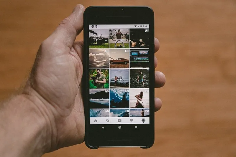 Hand holding a phone displaying an Instagram profile photo grid