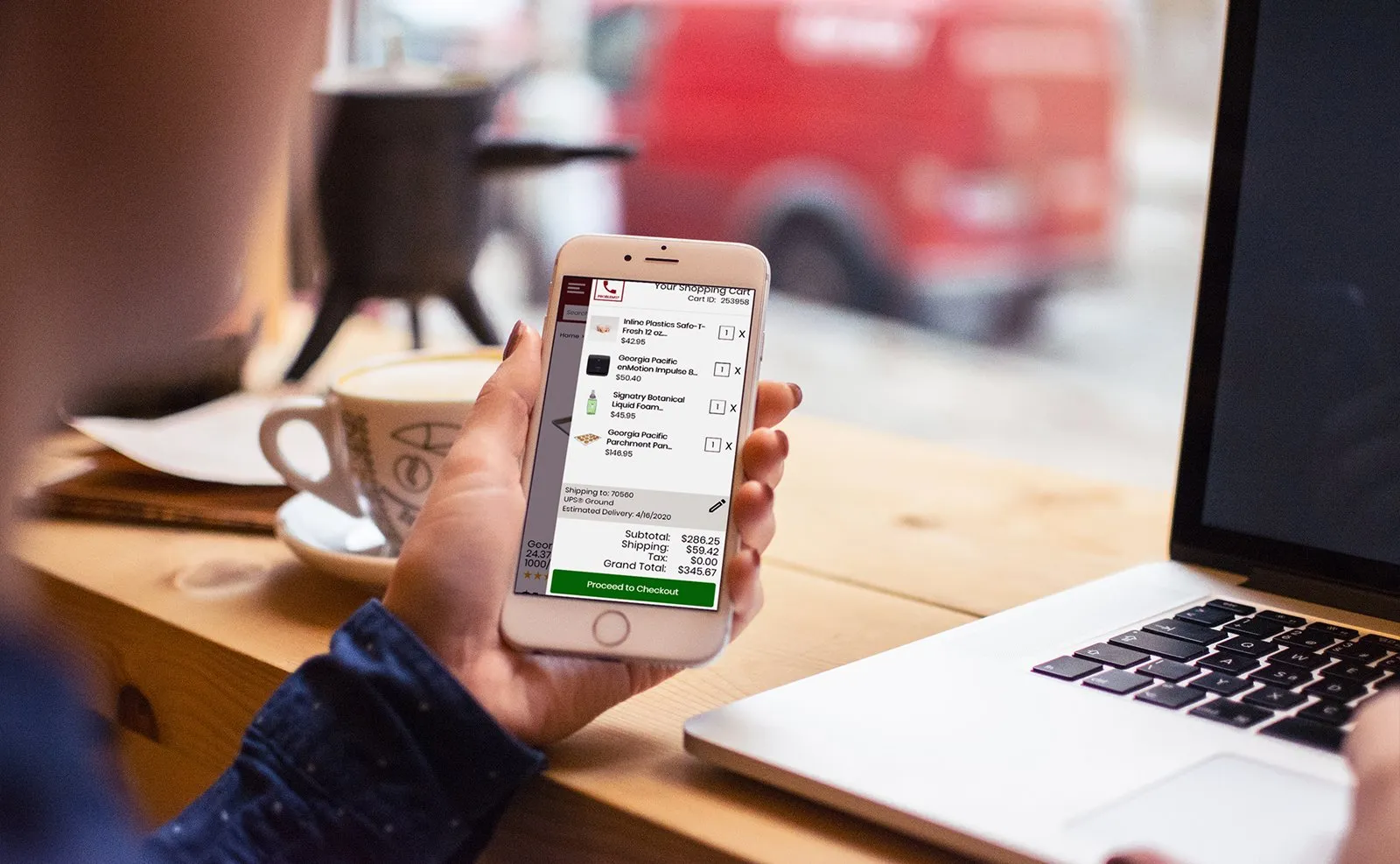 Hand holding a phone showing the PJP Go shopping cart with line items, shipping and a $345.67 grand total