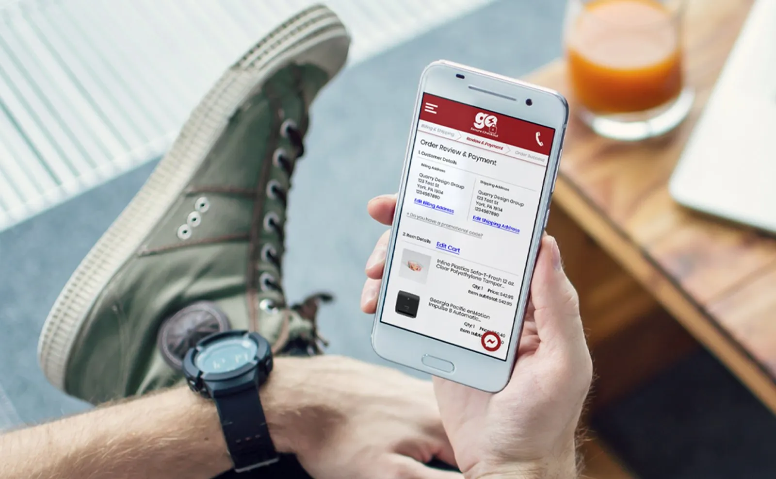 Hand holding a phone showing the PJP Go order review and payment screen with billing, shipping and item details